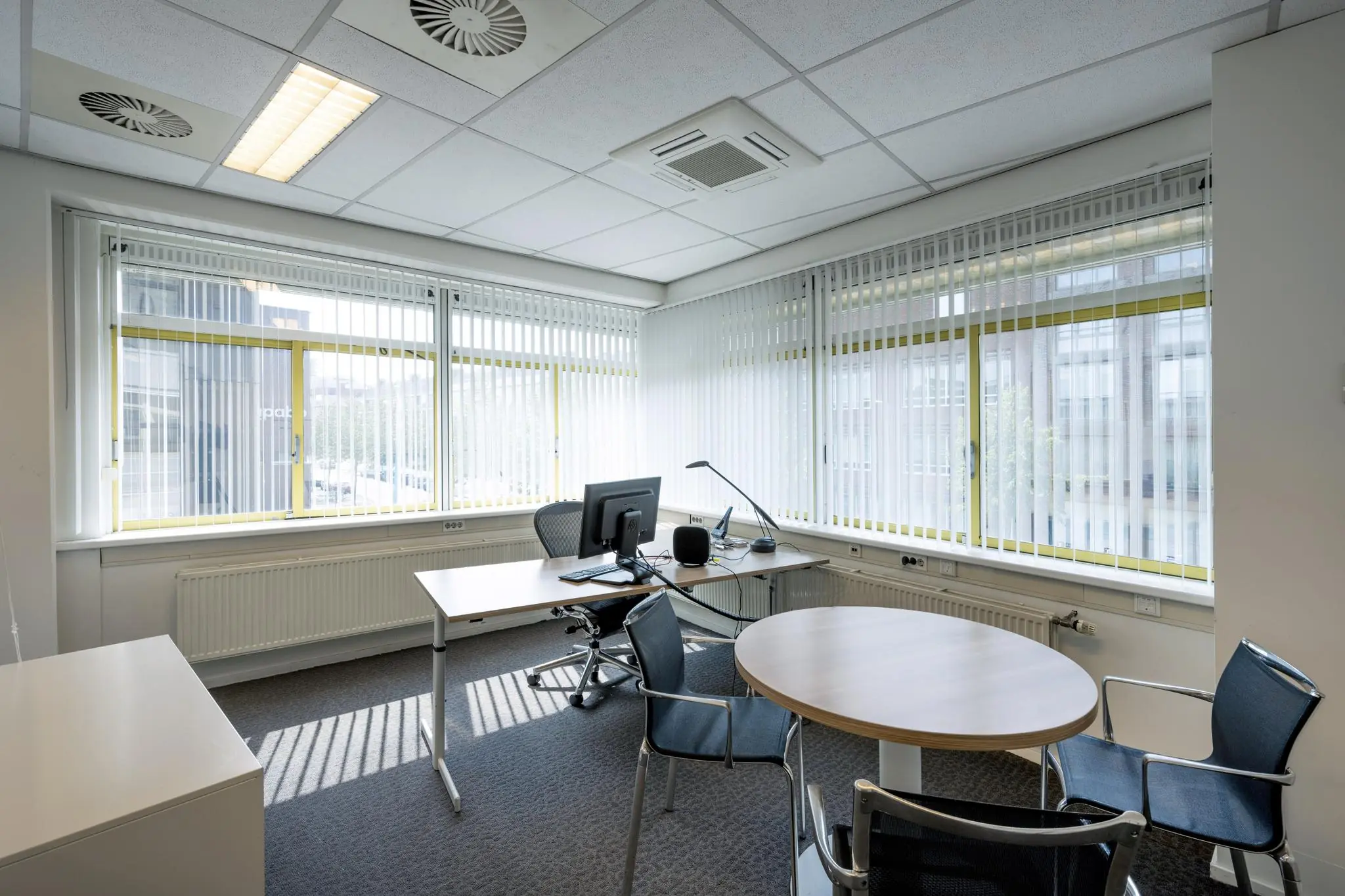 Modern ingerichte kantoorruimte aan de Jan Tooropstraat met bureaus, stoelen en grote ramen met verticale lamellen.